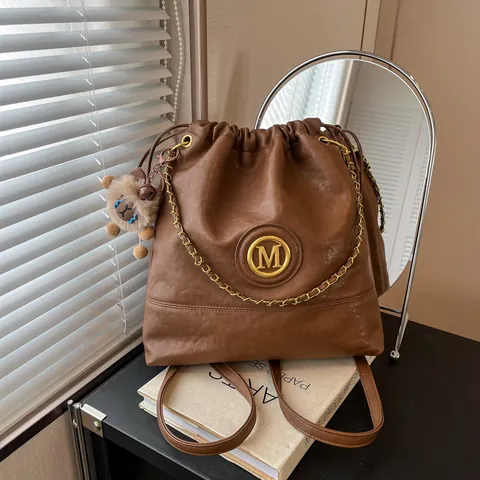 Sac Seau à Cordon en Cuir PU pour Femmes Grande Capacité Sac à Bandoulière Avec Décoration de Chaîne Logo M en Métal et Breloque en Peluche Sac Cabas Décontracté