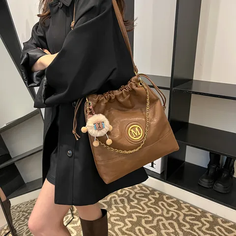 Sac Seau à Cordon en Cuir PU pour Femmes Grande Capacité Sac à Bandoulière Avec Décoration de Chaîne Logo M en Métal et Breloque en Peluche Sac Cabas Décontracté